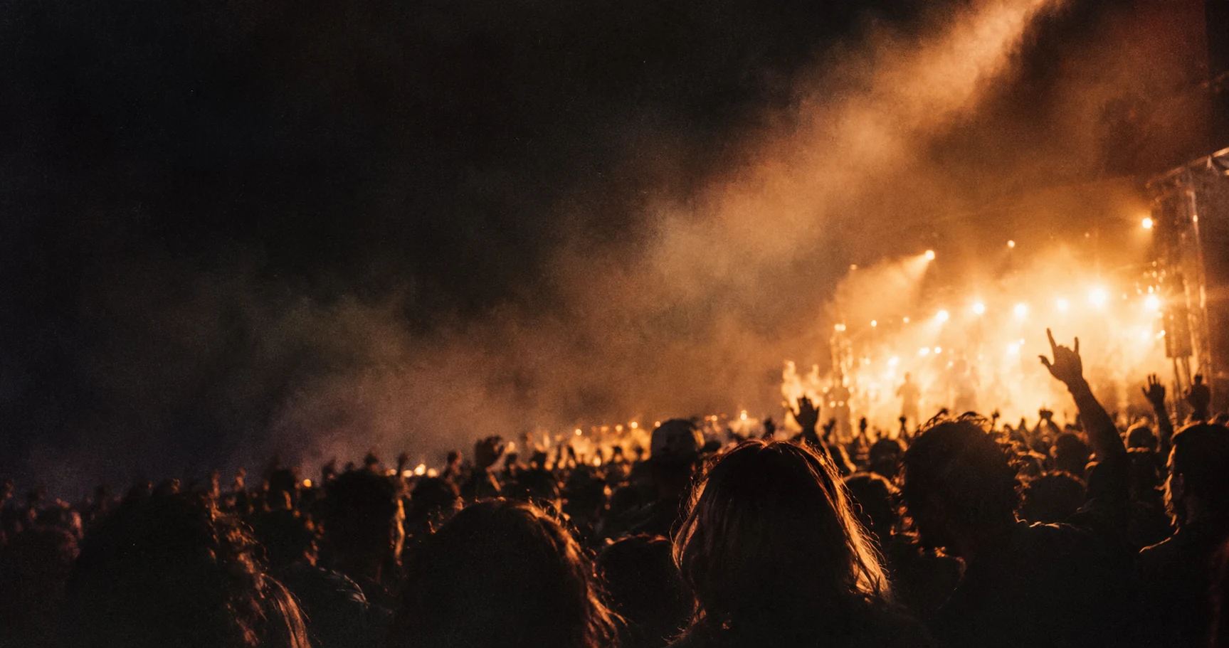 Concert crowd with hands raised under stage lights.
